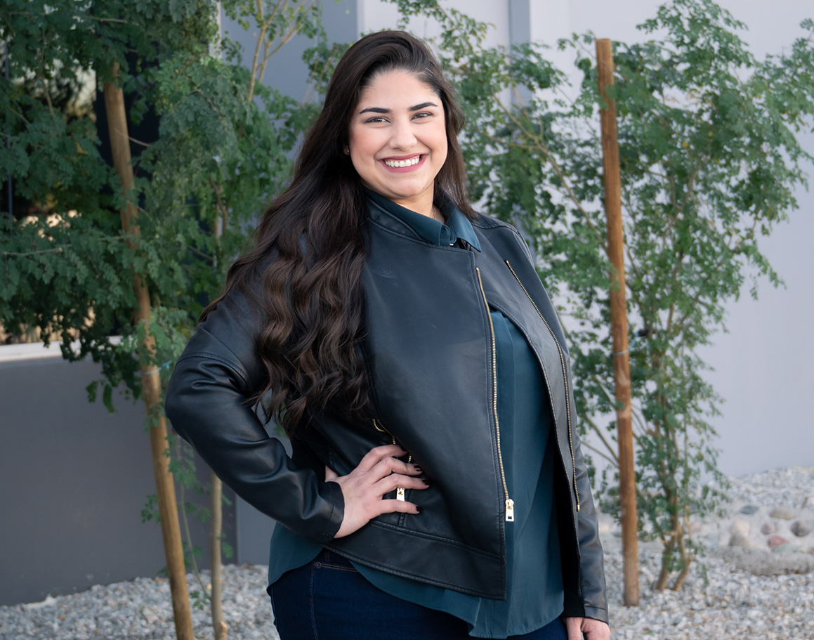 Mariellys Gutierrez smiling standing infront of small trees and building